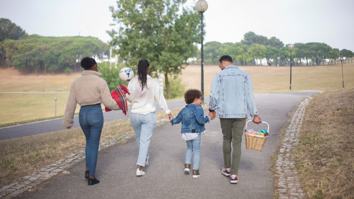 A family enjoys a peaceful walk in a picturesque park, holding hands and carrying a picnic basket.